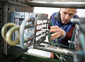 A process engineer checking on an injection molded part in a hot runner system.